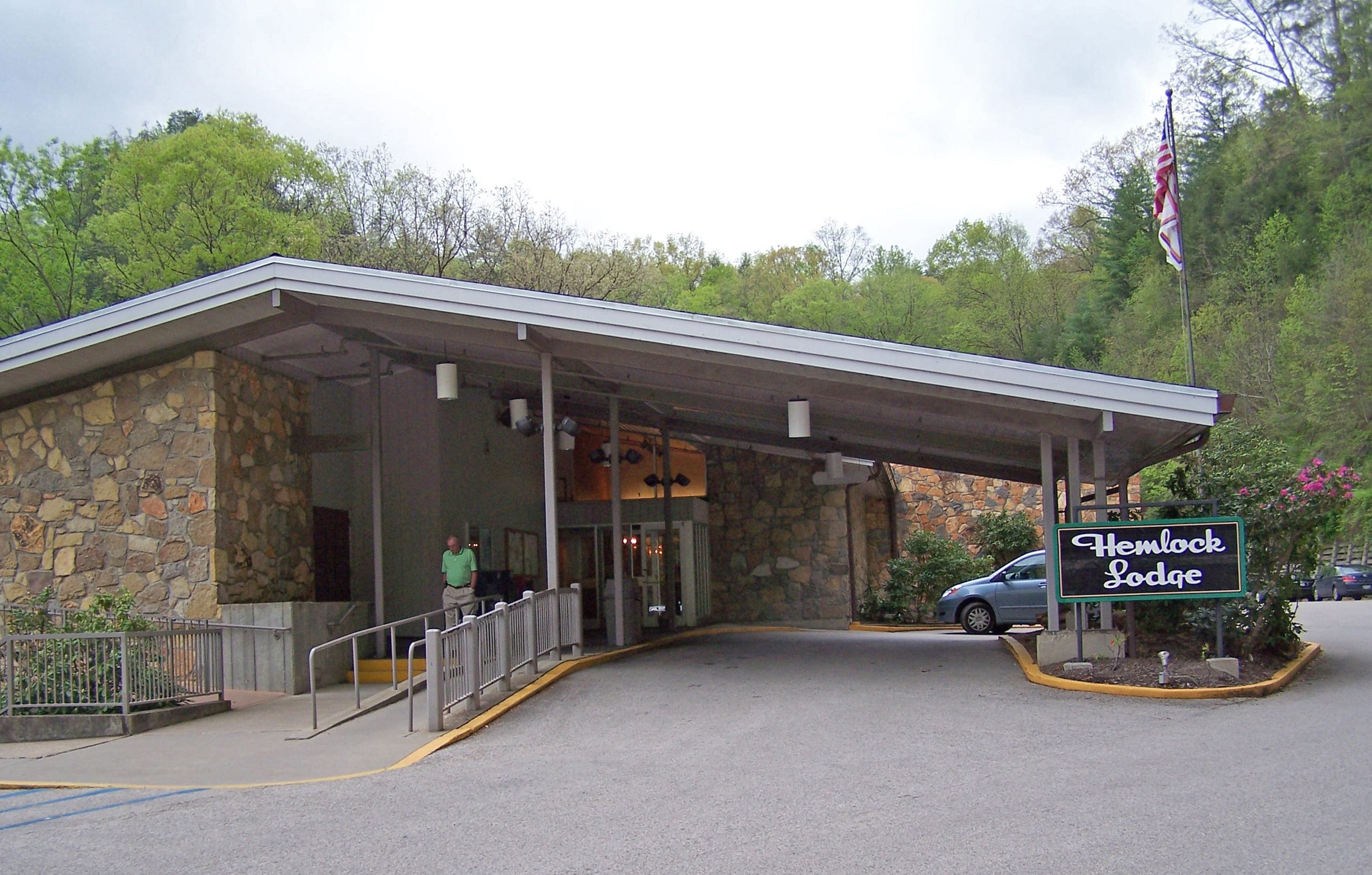 A stone building with a covered entrance, a sign reading "Hemlock Lodge," and an American flag.