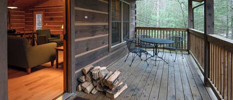 A wooden cabin with a porch, a dining area with a table and chairs, and a stack of firewood.