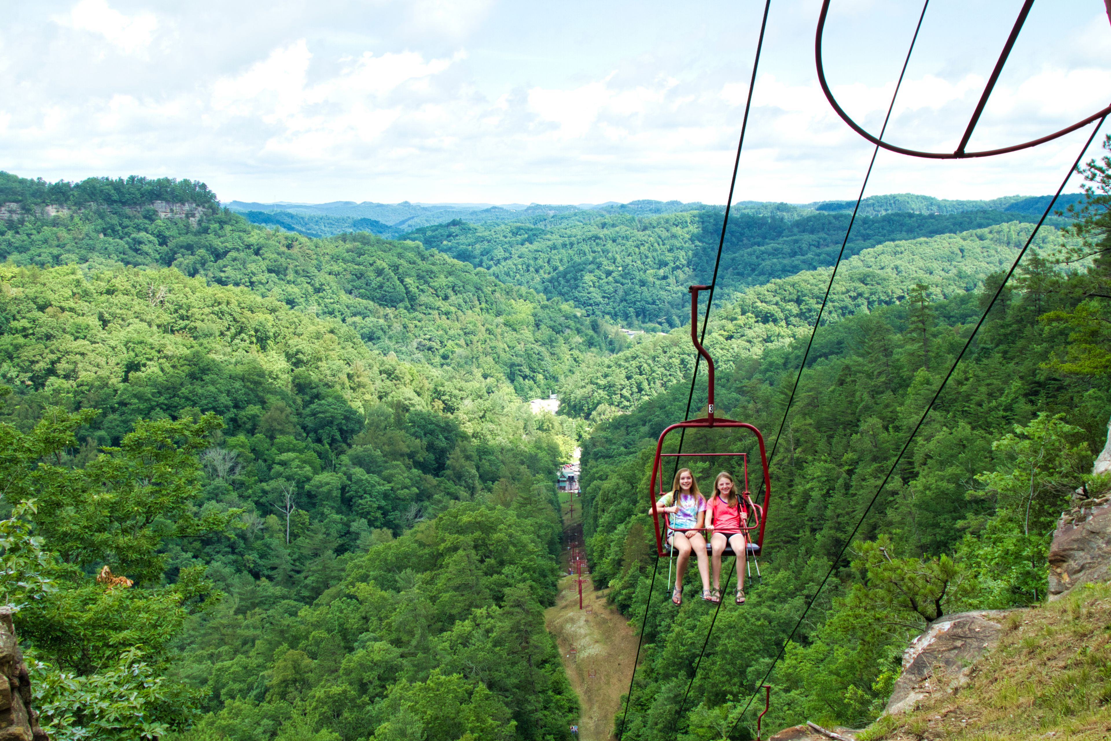 A cable car with two passengers over a forested valley.