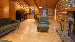 A log cabin interior with a wooden floor, a sofa, a chair, a dining table, and a stone fireplace. - Natural Bridge State Resort Park (Slade)