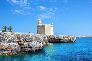 A coastal stone tower with a flag, surrounded by clear blue water and rocky cliffs.