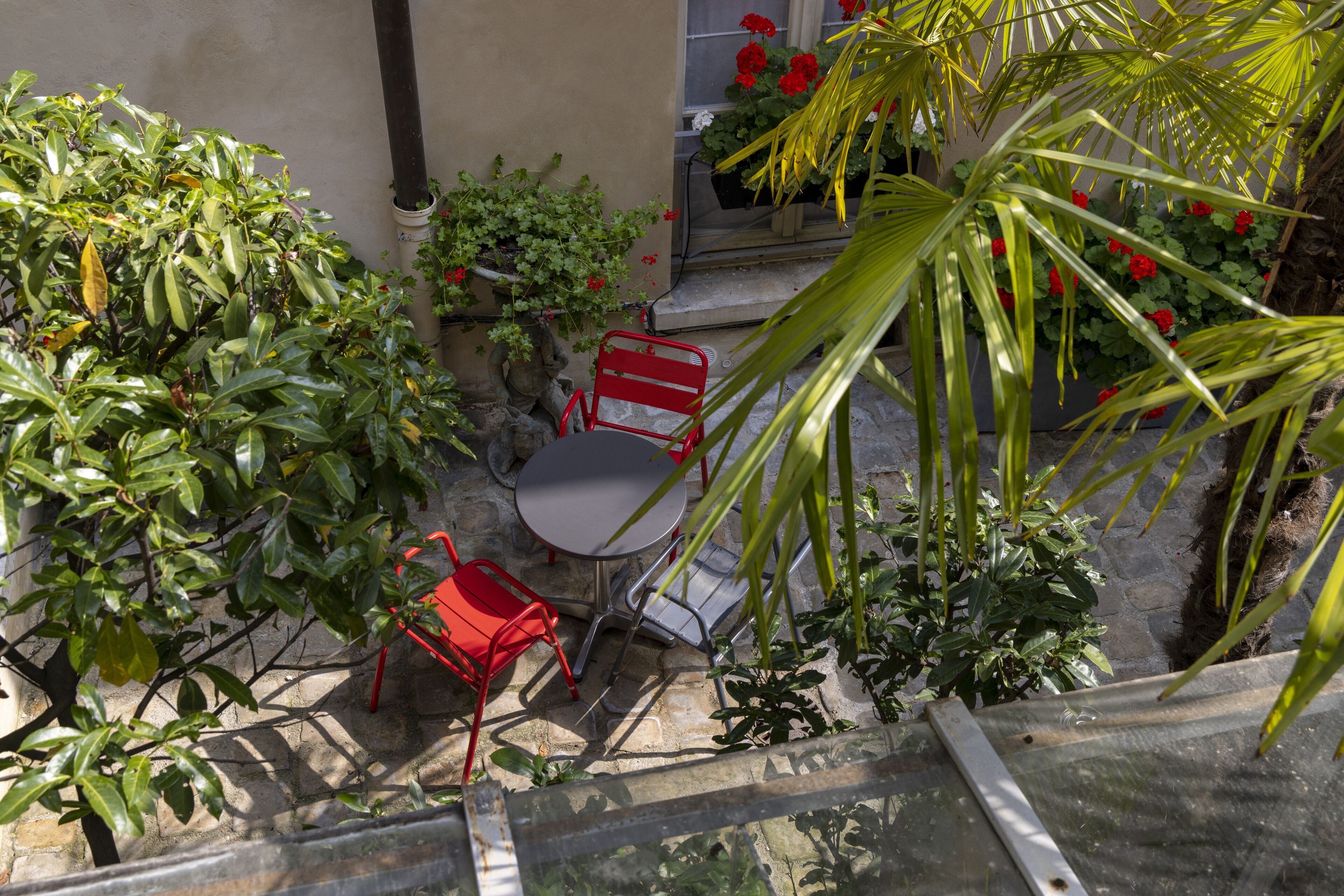 Un pequeño patio al aire libre con una mesa y sillas, rodeado de plantas y flores diversas.
