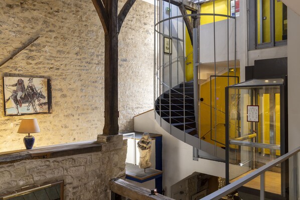 A multi-level interior with exposed brick walls, a spiral staircase, and a statue. - Hotel du Jeu de Paume (Paris)