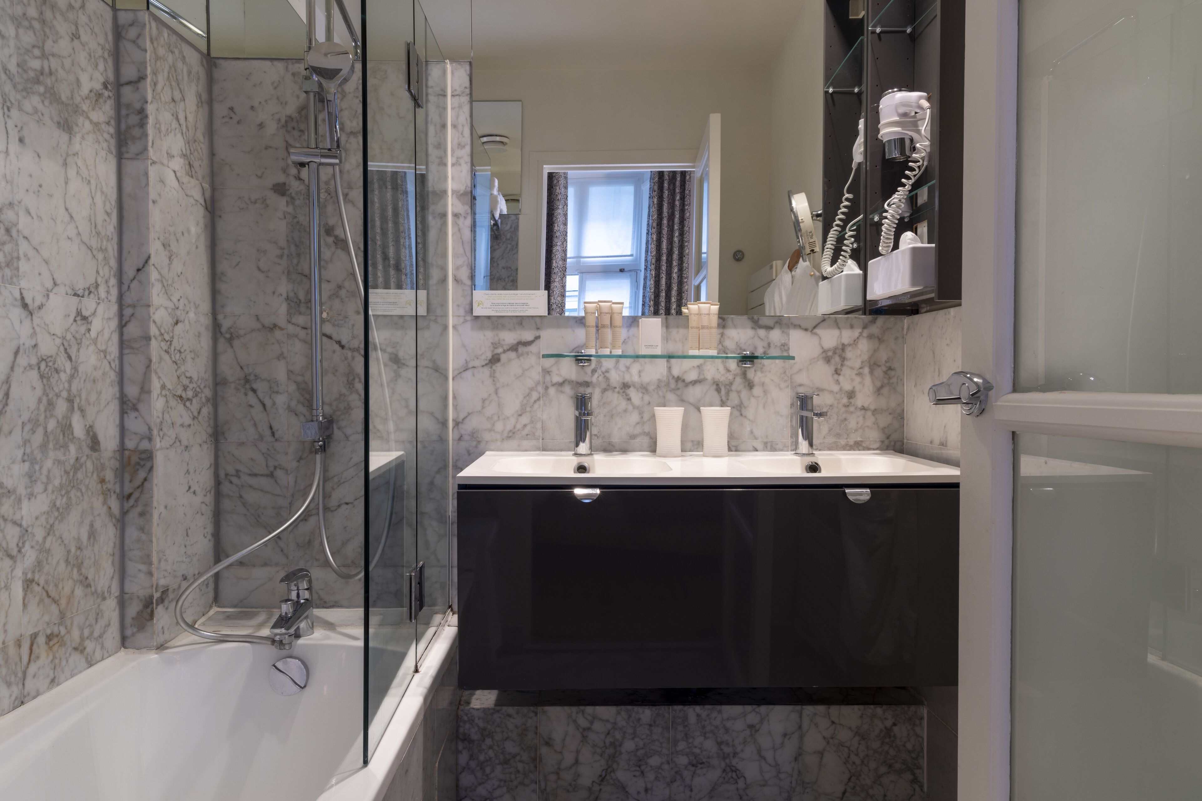Un baño moderno con cabina de ducha de vidrio, tocador negro con espejo y salpicadero de mármol.