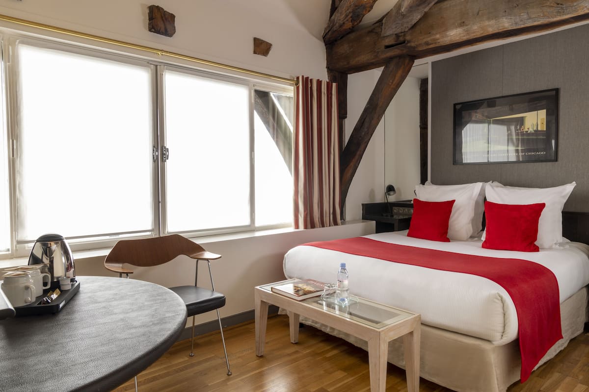 Une chambre d’hôtel avec un lit, une table avec une bouilloire, une chaise et une fenêtre avec des rideaux.