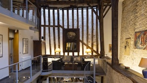 Ein geräumiger Innenraum mit hoher Decke, freiliegenden Holzbalken, einem Essbereich mit vier gedeckten Tischen und einem Kamin.