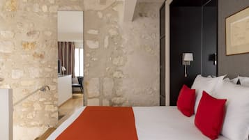 Quarto com parede de pedra, cama com roupa de cama branca e vermelha, e uma luminária moderna.