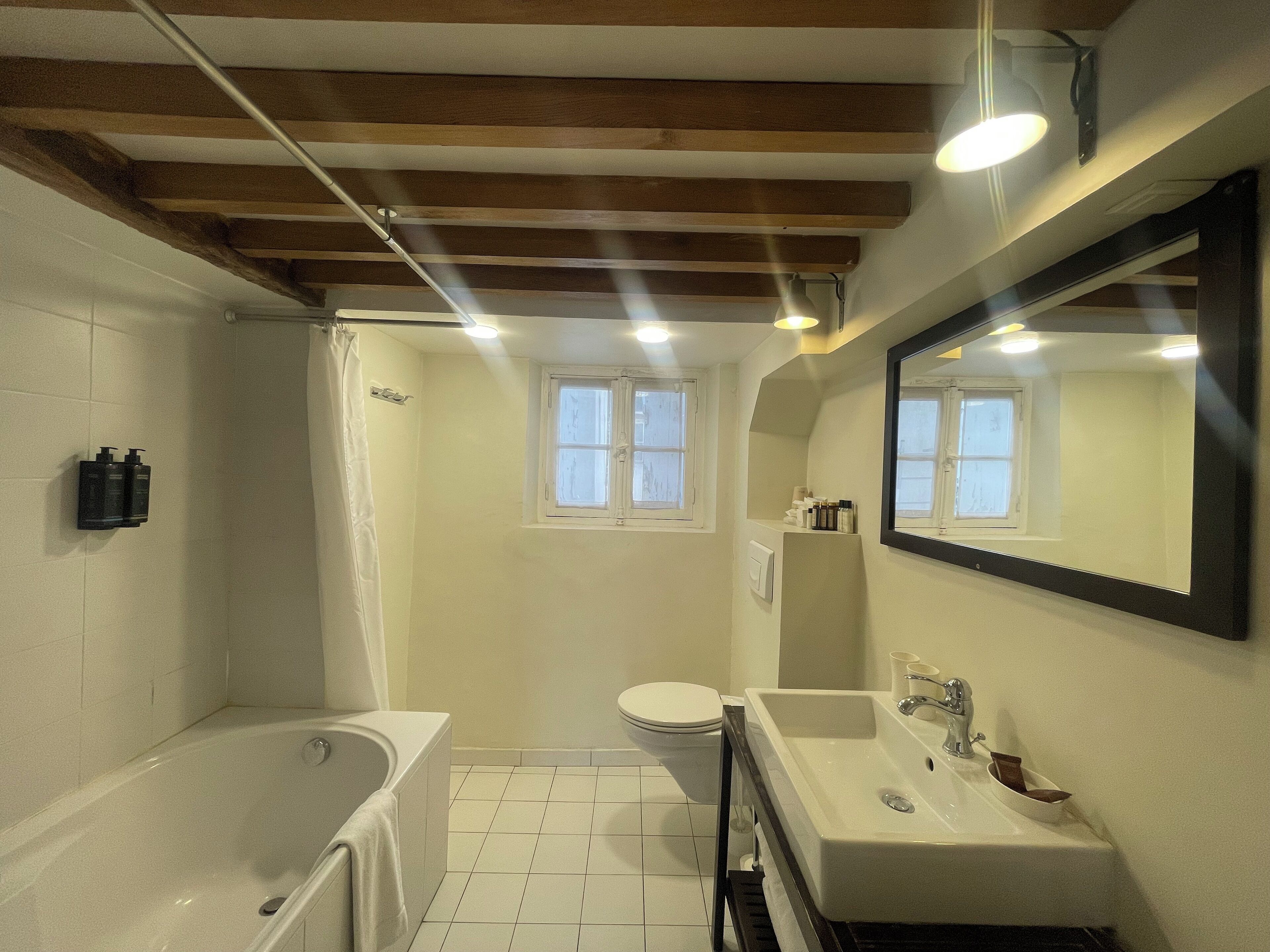 Een badkamer met bad, toilet en wastafel, met houten balken in het plafond en een raam.