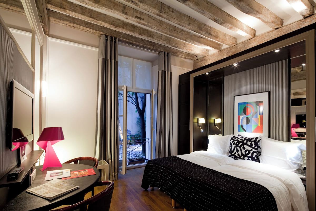 Une chambre d’hôtel avec un lit, un bureau avec une lampe, une chaise, une télévision et une grande fenêtre.