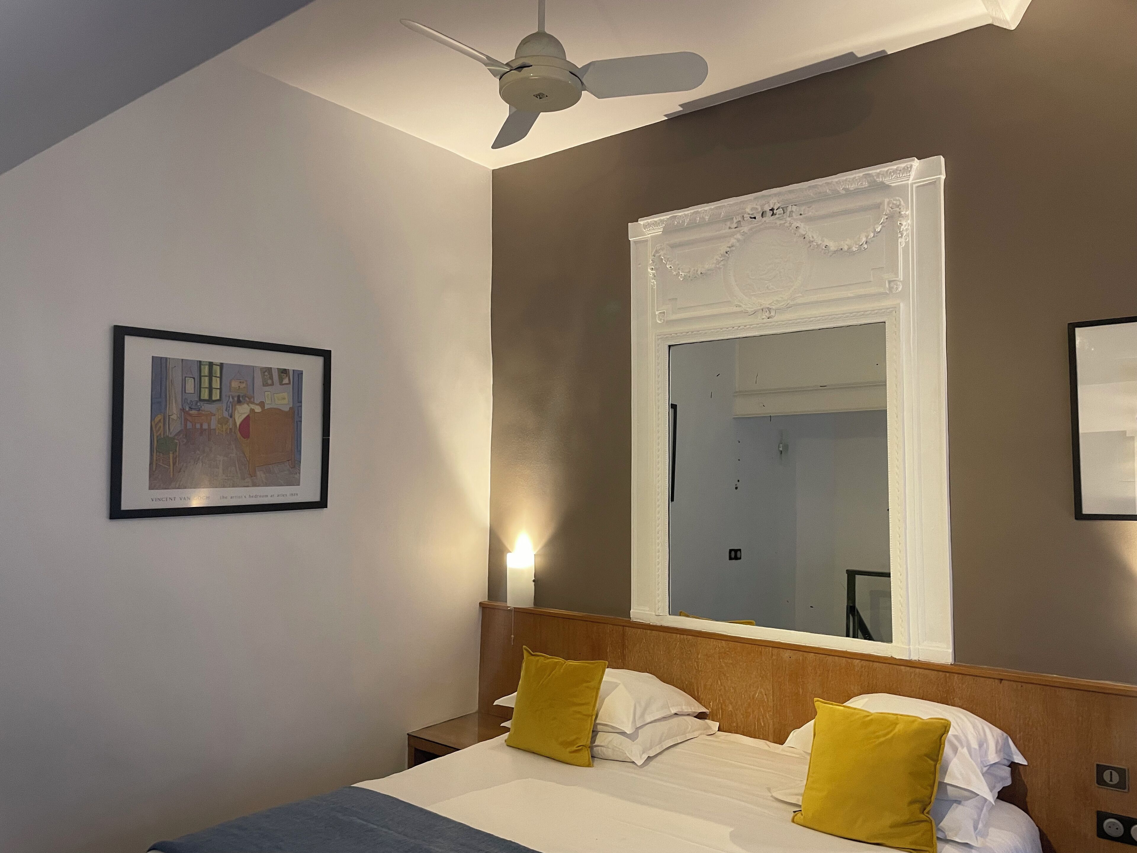 A hotel room with a bed, a large mirror, a ceiling fan, and a framed picture on the wall.