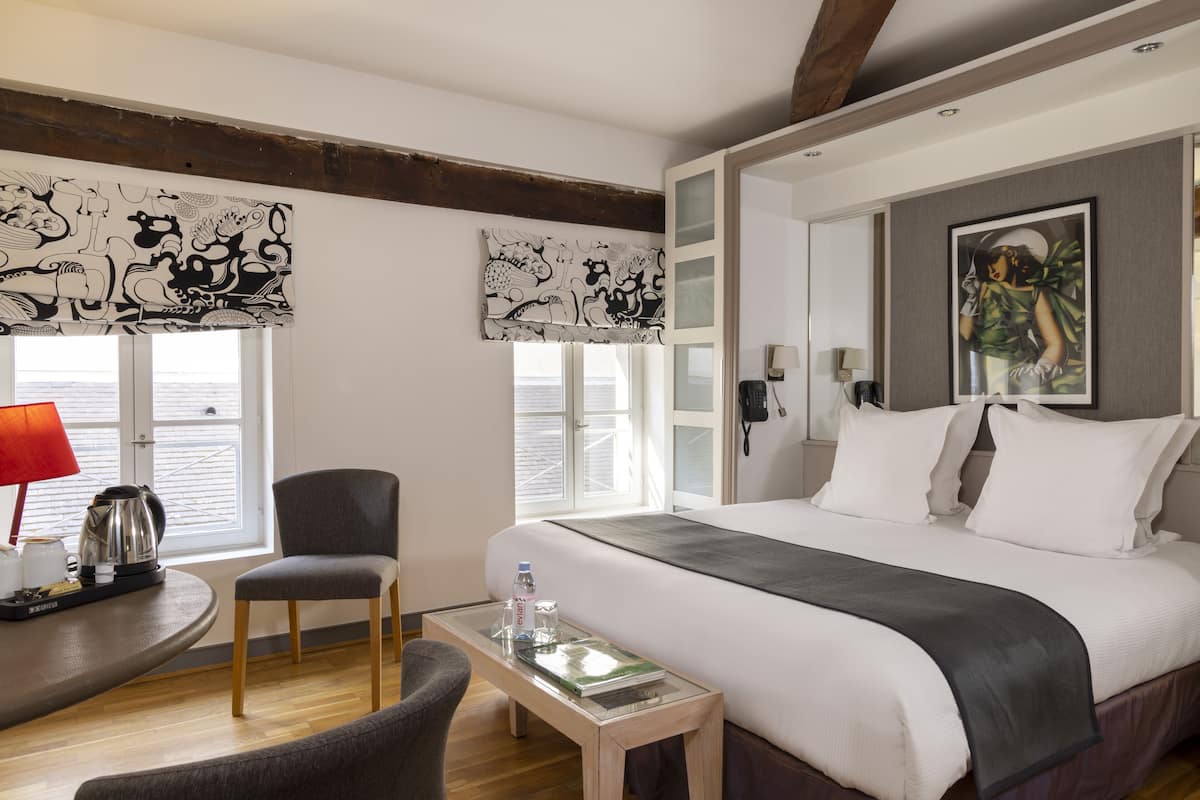 Une chambre d’hôtel avec un grand lit, une chaise, une petite table et des œuvres d’art accrochées aux murs.