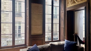Ein Zimmer mit einer Couch, einem großen Fenster mit Blick auf Gebäude und einer dekorativen Decke.