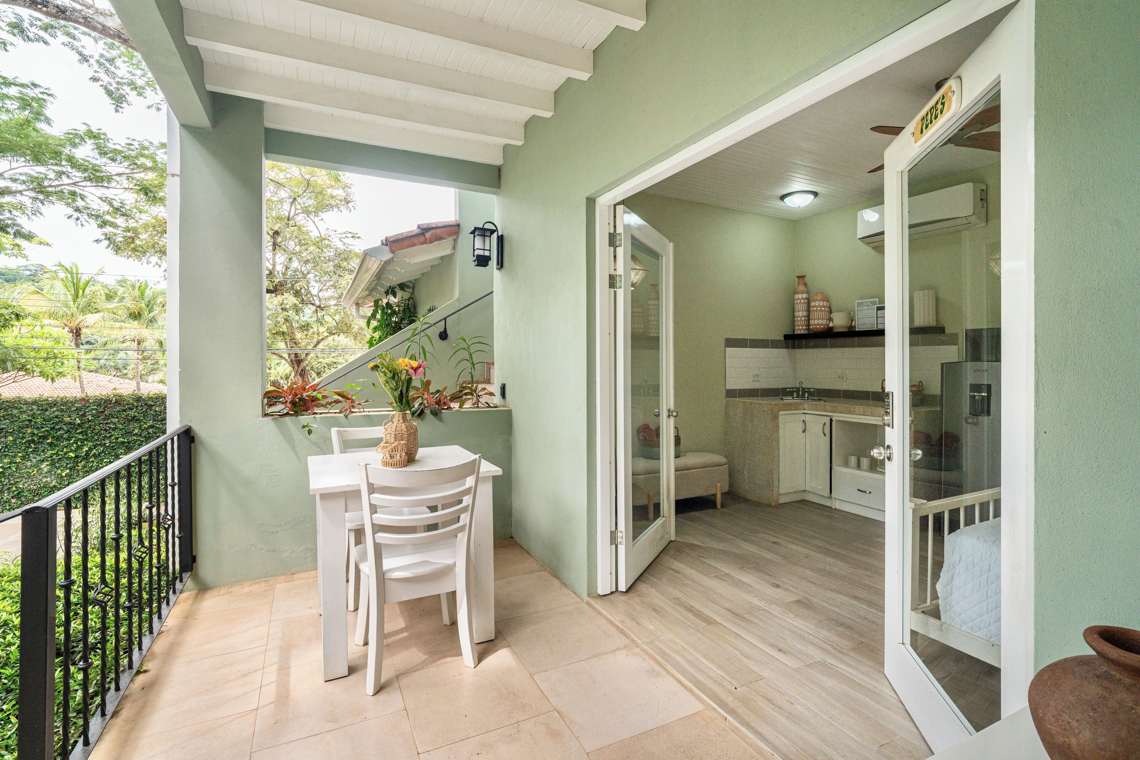 Un balcon avec une table et des chaises, un coin cuisine équipé de placards et d’un réfrigérateur, et une porte donnant sur une autre pièce.
