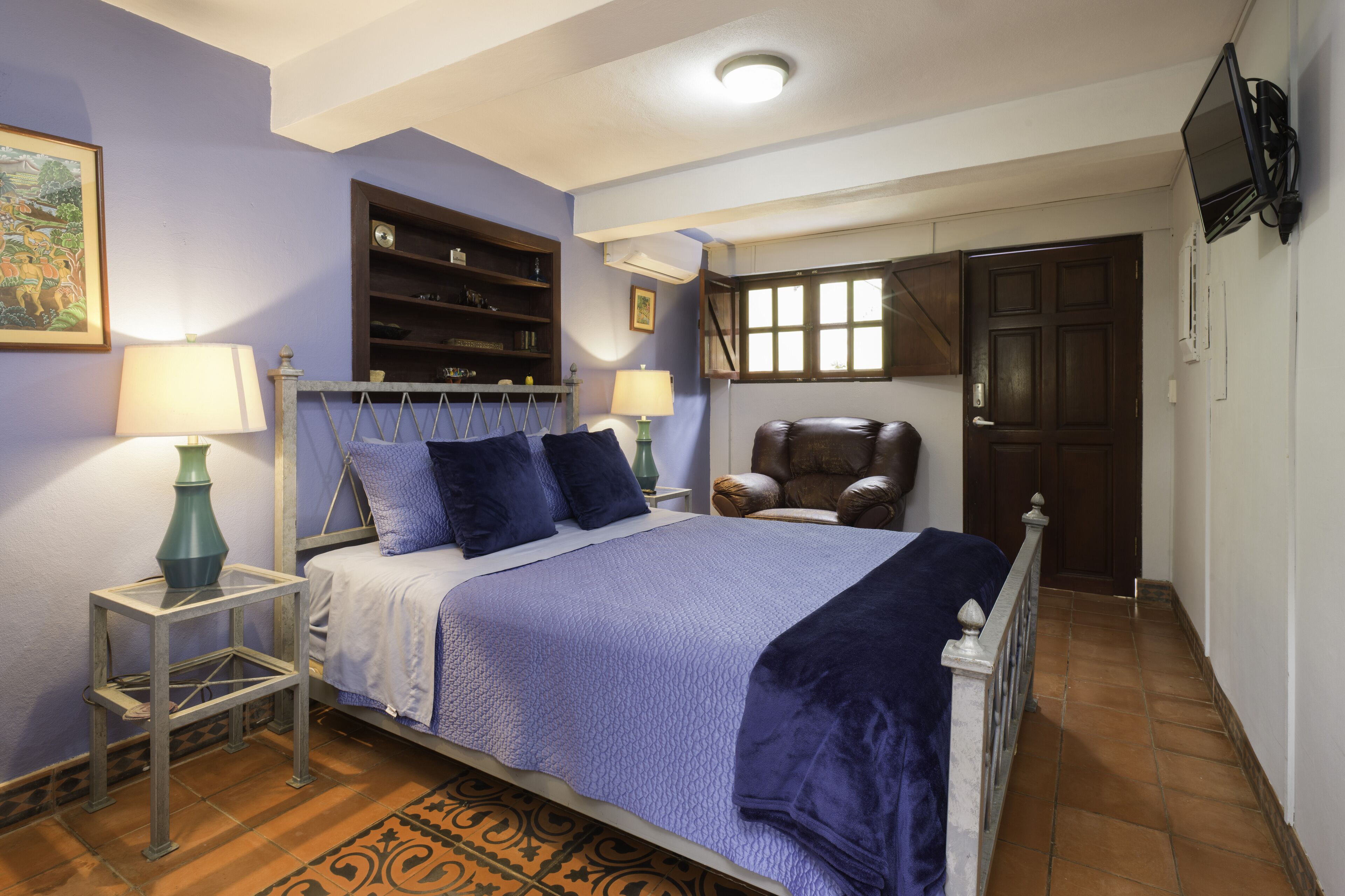 A bedroom with a bed, two bedside tables, a chair, a wardrobe, a television, and a door.
