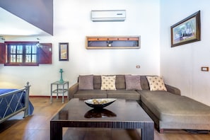 A living room with a sofa, a coffee table, a window with a view, and an air conditioning unit. - Casa Leona (Tamarindo)