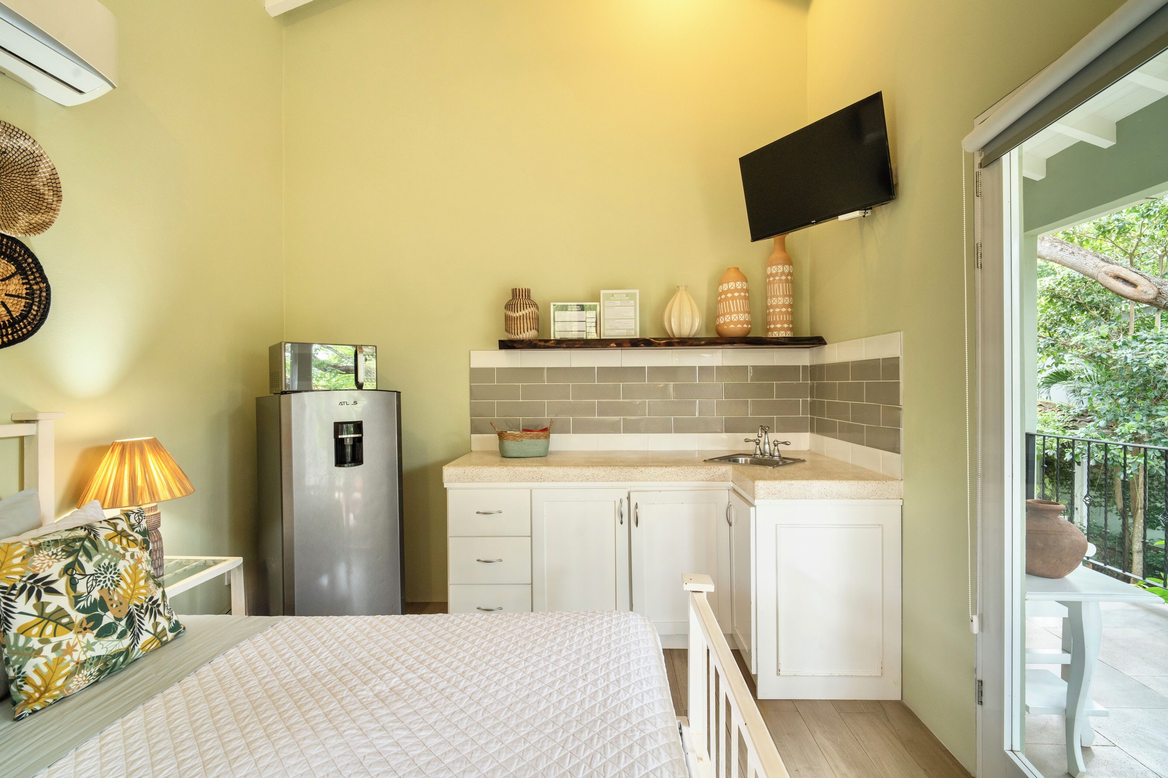 Una kitchenette compacta con refrigerador, lavamanos y un televisor de pantalla plana montado arriba.