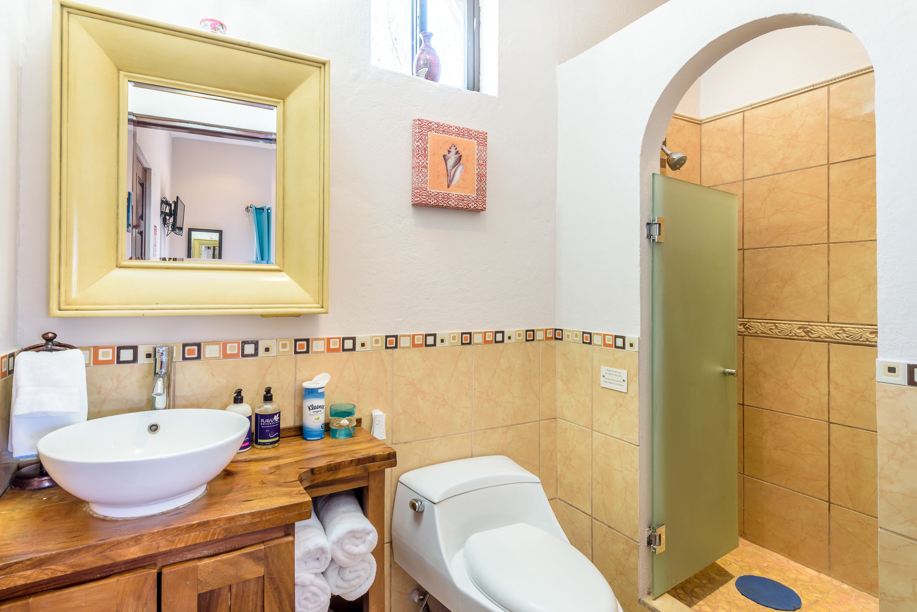 Un baño con un lavamanos grande de color blanco, un inodoro, una ducha y un espejo sobre el lavamanos.