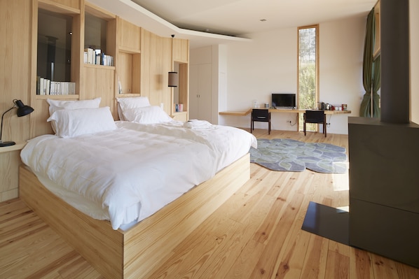 A modern bedroom with a large bed, wooden headboard, built-in shelves, a desk, and a television.