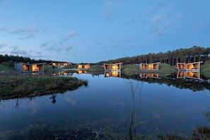A series of modern, wooden cabins with large windows, situated on a lakeside with reflections.