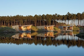 Three modern wooden cabins by a calm lake, surrounded by a forest.