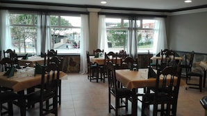 A dining area with multiple tables and chairs, large windows with curtains, and a view of the street outside. - Hotel Pozo De La Nieve (Tordesillas)
