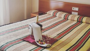 Ein Hotelzimmer mit einem Bett, einem Nachttisch, einer Fernbedienung, einer Champagnerflasche und einem dekorativen Kissen.