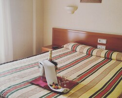 Quarto de hotel com cama, mesa de cabeceira, controle remoto, garrafa de champanhe e travesseiro decorativo.