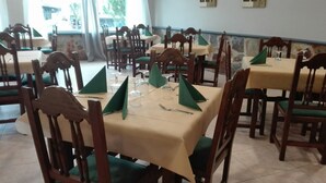 Ein Essbereich mit mehreren Tischen und Stühlen, jeder Tisch ist mit grünen Servietten und Weingläsern gedeckt.
