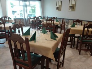 Un comedor con varias mesas y sillas, cada conjunto con servilletas verdes y copas de vino.