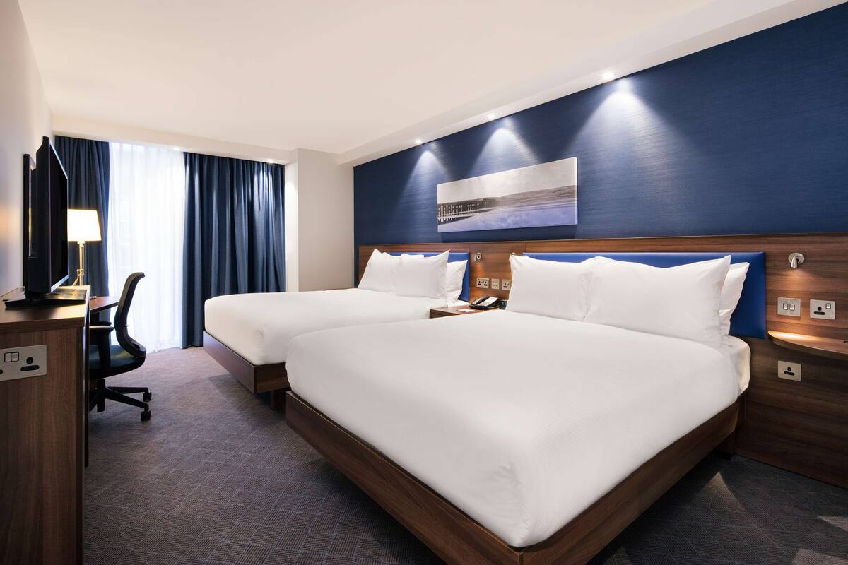 A hotel room with two beds, a desk, and a chair.
