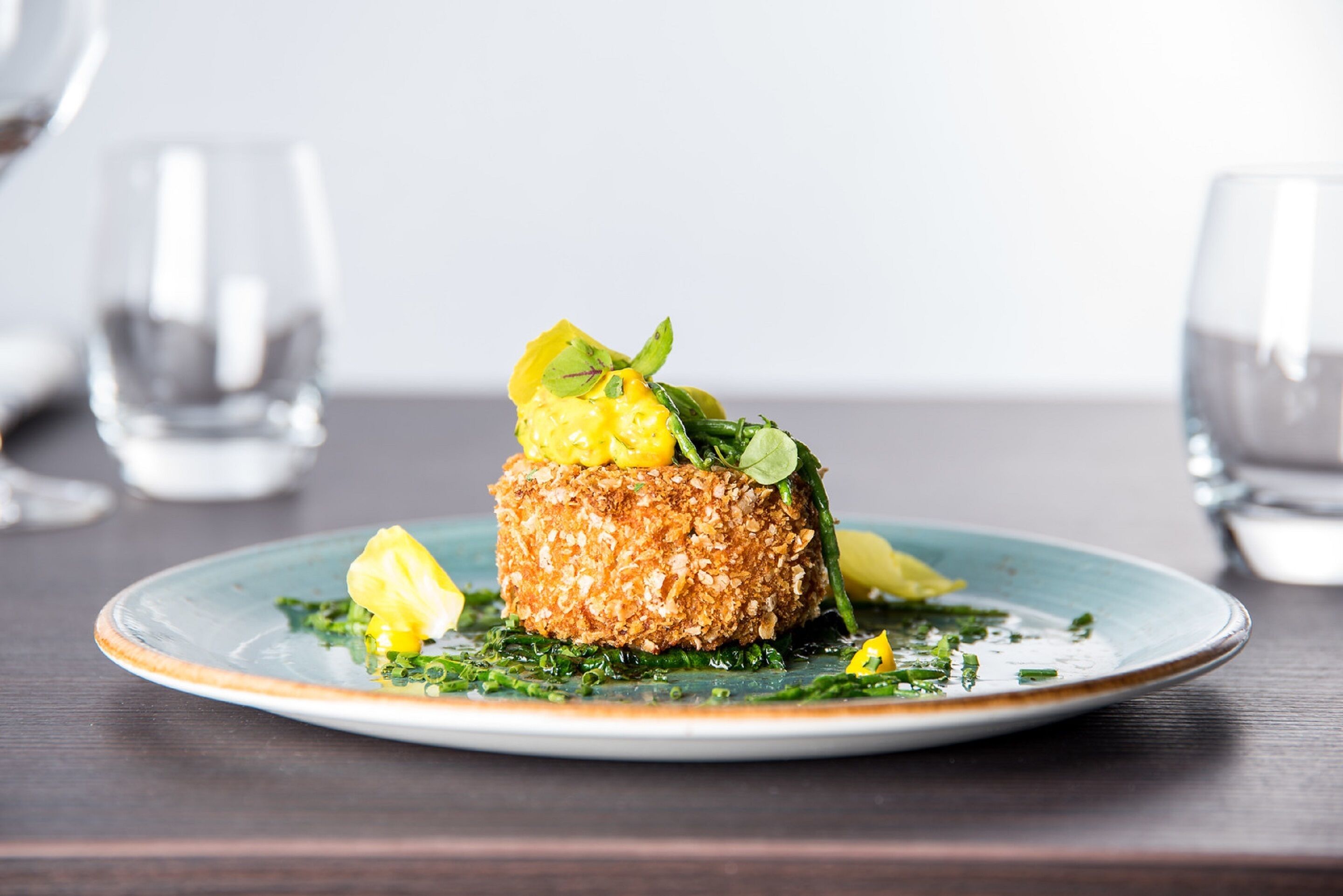 Un plato con costra dorada, decorado con hojas verdes y rodajas de limón, sobre un plato con borde azul.