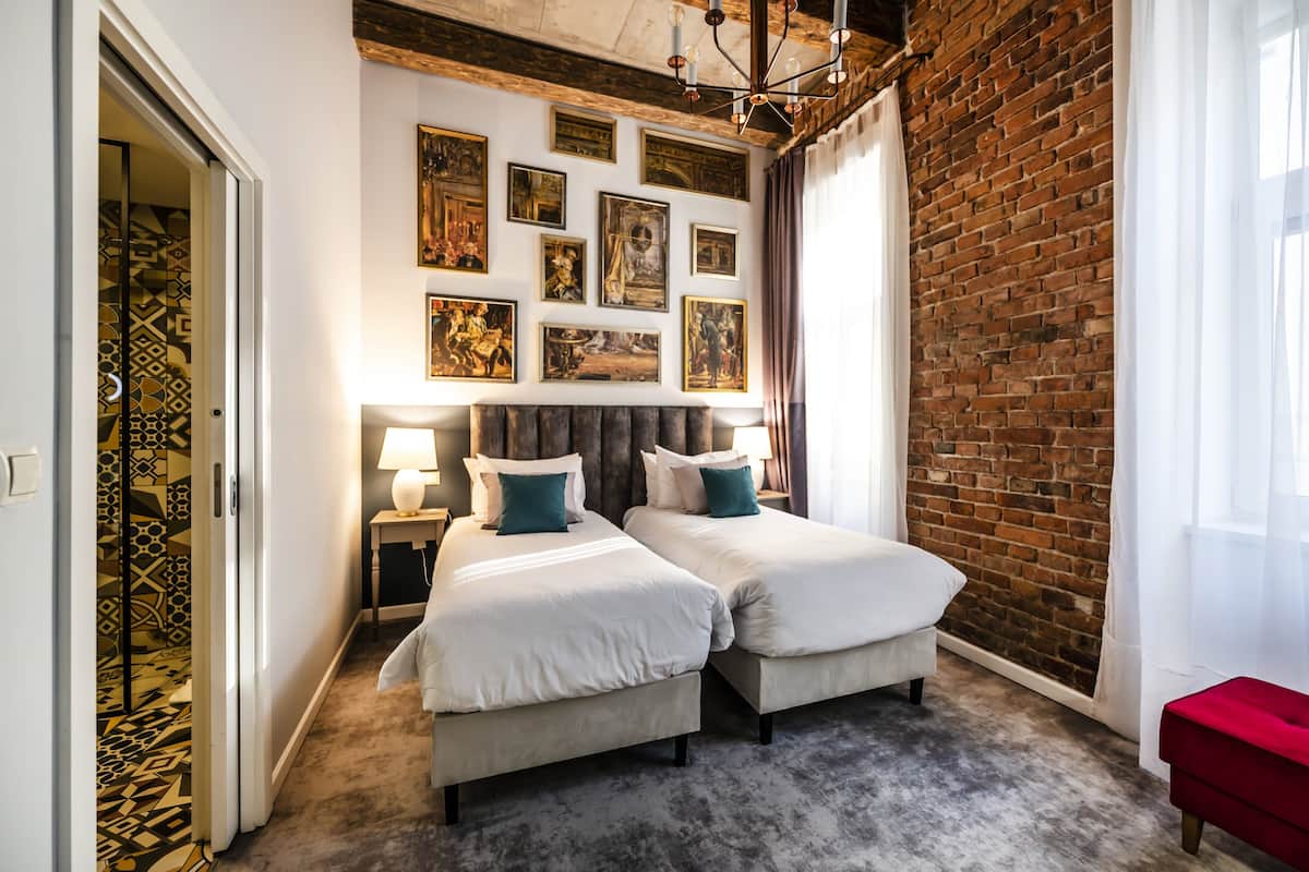 Ein Hotelzimmer mit zwei Betten, einer Ziegelwand und einer Bildergalerie an der Wand.