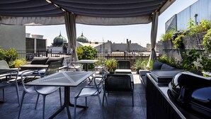 Une terrasse extérieure avec des tables et des chaises, un barbecue et des plantes en pot.