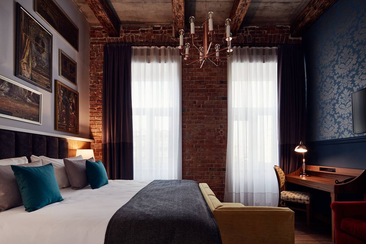 Ein Hotelzimmer mit einem großen Bett, einem Schreibtisch, einem Stuhl und einem Fernseher an der Wand.
