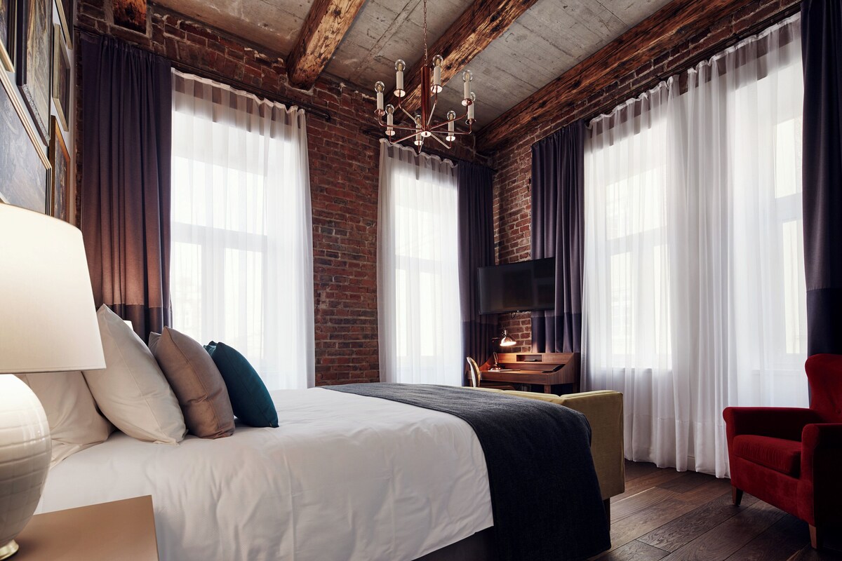 Une chambre d’hôtel moderne avec un grand lit, une cheminée et de grandes fenêtres équipées de rideaux.