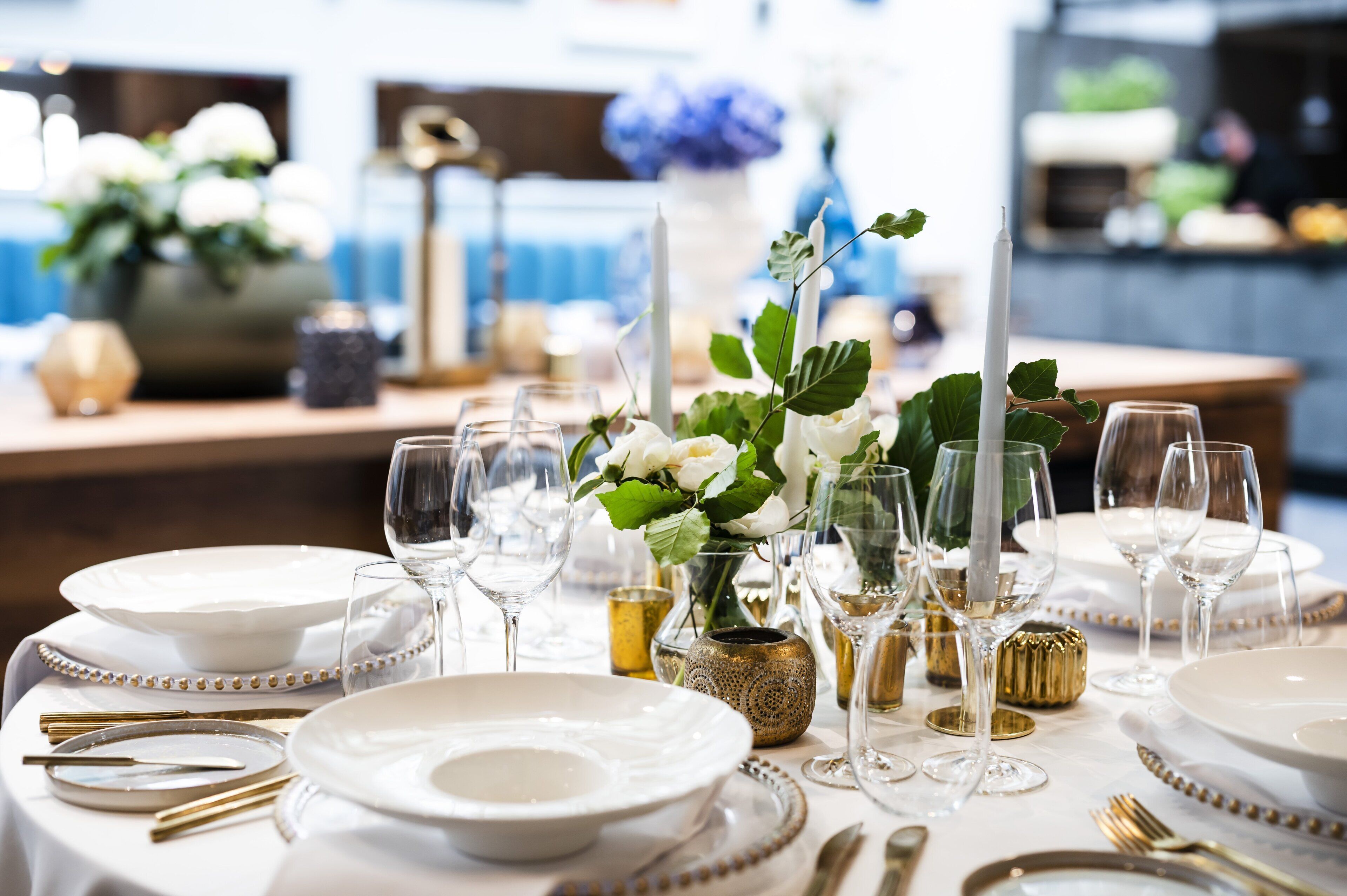 Mesa dispuesta para un evento de cena formal, con platos blancos, cubiertos dorados y copas de cristal.