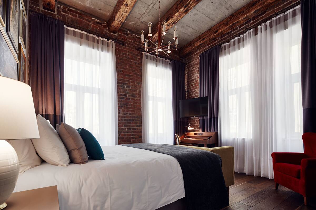 Ein modernes Hotelzimmer mit einem großen Bett, einem Kamin und großen Fenstern mit Vorhängen.