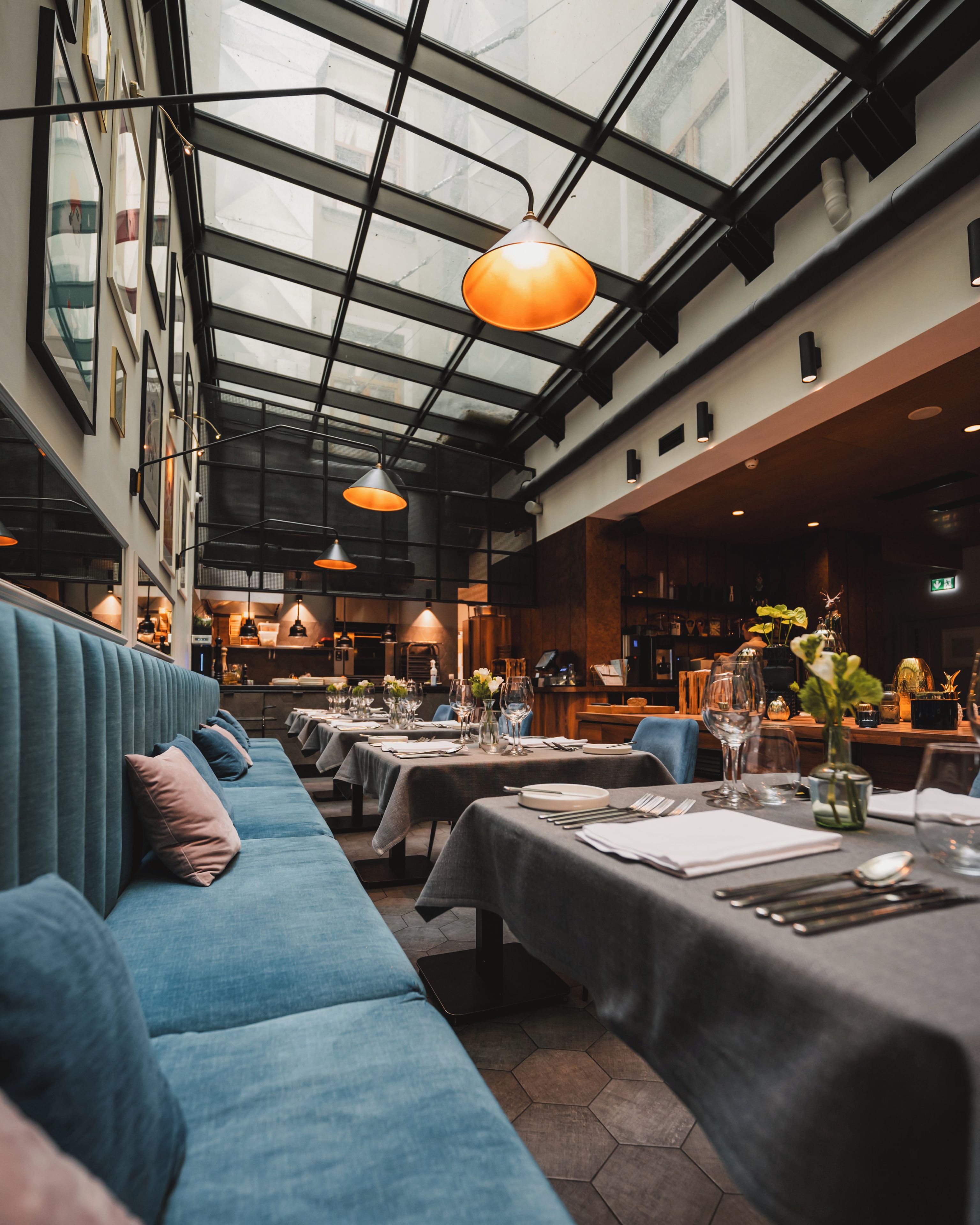 Restaurante com um sofá comprido azul, mesas preparadas para refeições e iluminação pendente.