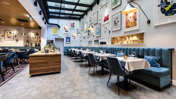A restaurant with hexagonal tile flooring, a central wooden counter, blue upholstered booths, and a variety of framed artwork on the walls.
