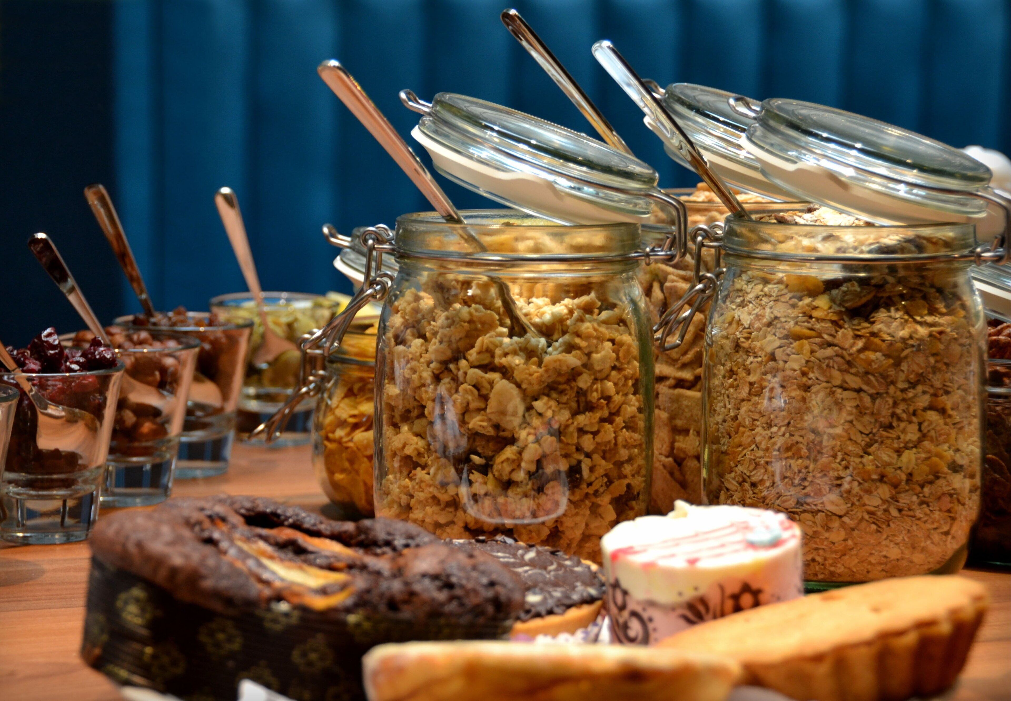 A buffet table with various food items including jars of granola, a chocolate cake, and a pastry.