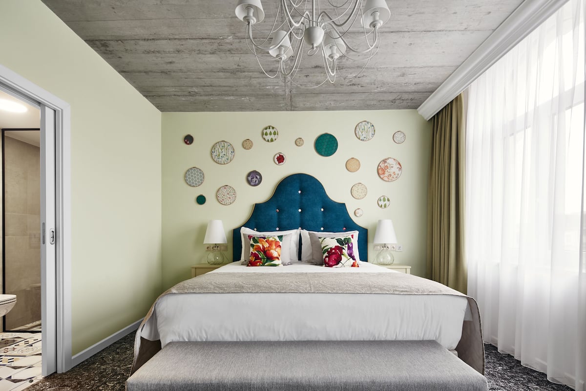 Ein Hotelzimmer mit einem großen Bett, einer Bank, einer Chandelüster und einer Wand, die mit runden Tellern verziert ist.