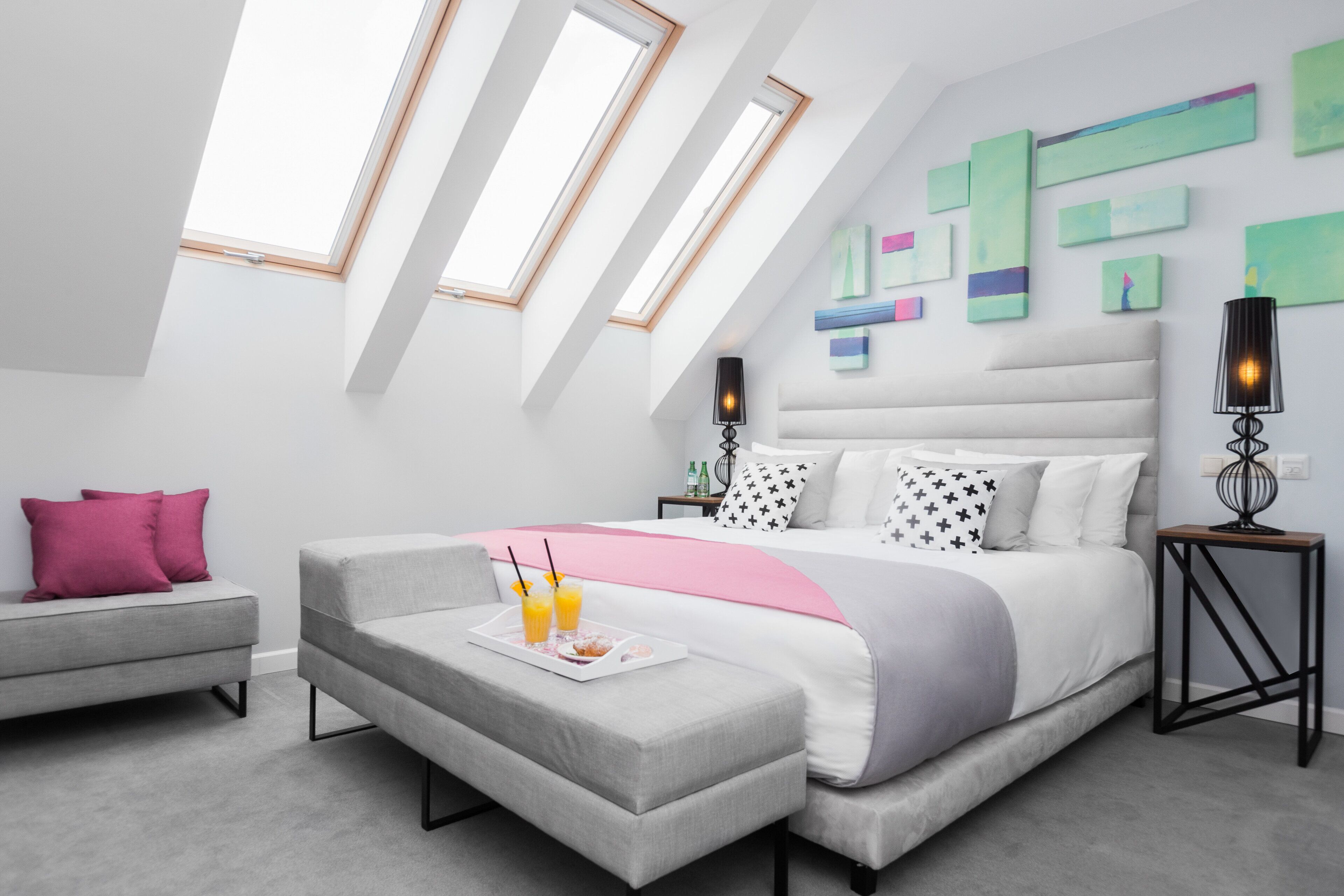 A modern bedroom with a large bed, a grey sofa, and a dining table with drinks.