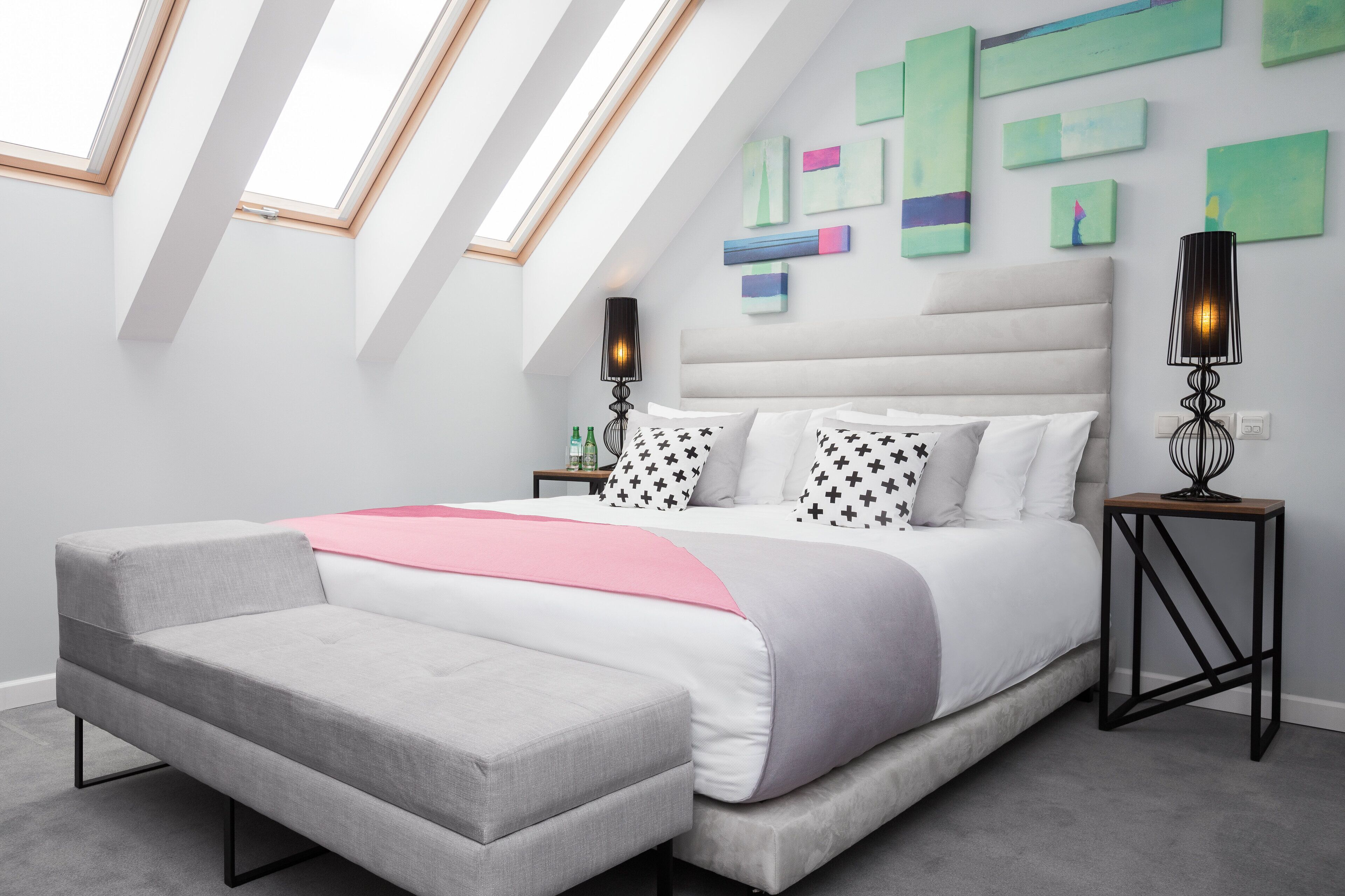A modern bedroom with a large bed, a grey bench, and a skylight.