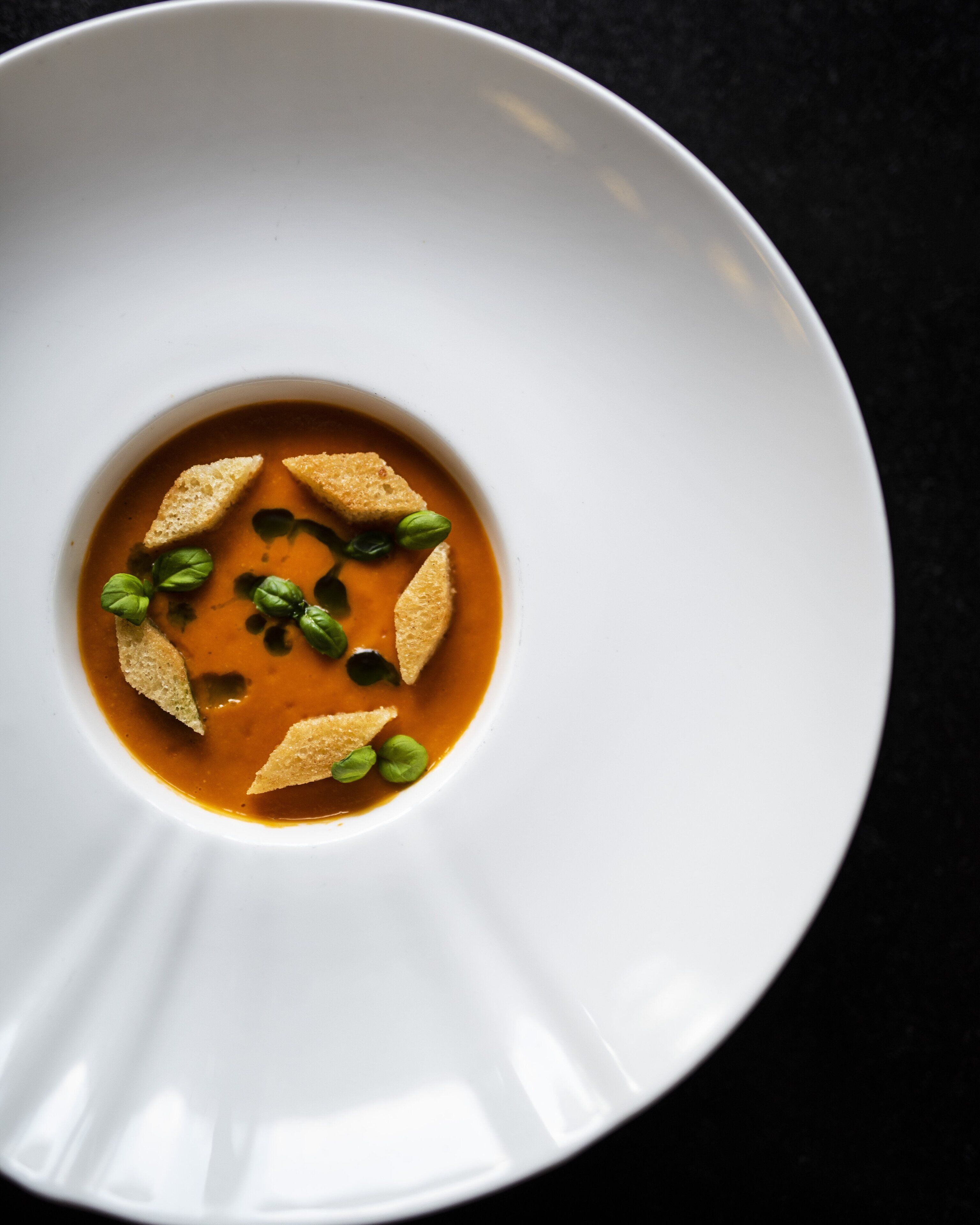 A white plate with a soup and garnishes.