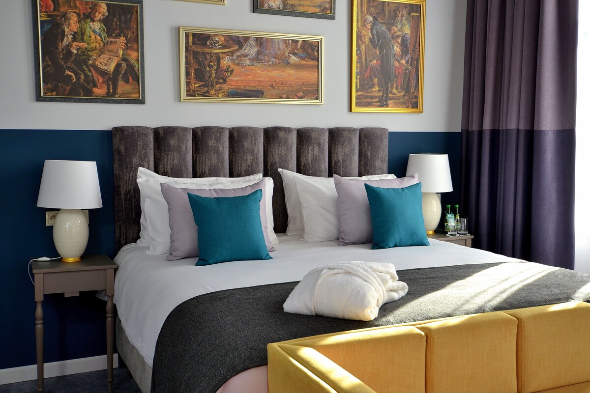 Une chambre d’hôtel avec un grand lit, deux tables de chevet et des œuvres d’art accrochées aux murs.