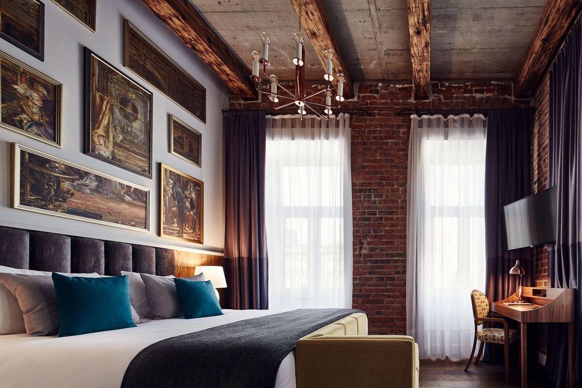 Ein Hotelzimmer mit einem großen Bett, einem Schreibtisch mit Stuhl, einem Fernseher und Bildern an den Wänden.