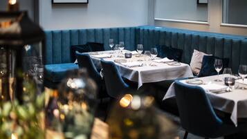 A restaurant with tables set for dining, a blue cushioned bench, and a framed picture on the wall.