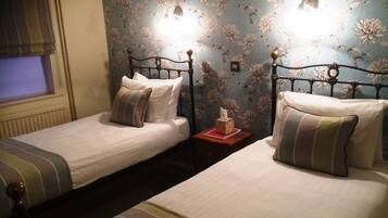Two single beds with metal frames, a bedside table with a tissue box, and a window with blinds.
