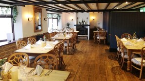 A restaurant with wooden tables and chairs, a fireplace, and wall-mounted lighting. - The Marquess Of Exeter (Oakham)