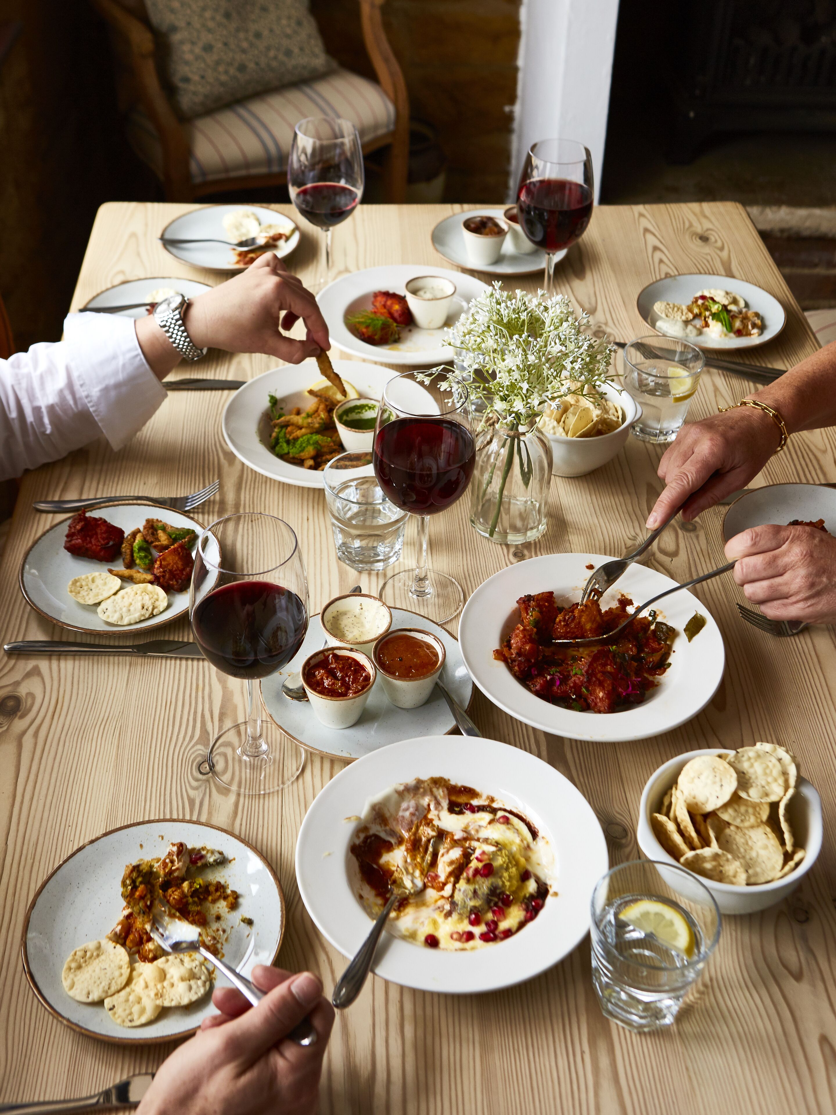 Une table à manger avec différents plats, des verres de vin et un vase rempli de fleurs.